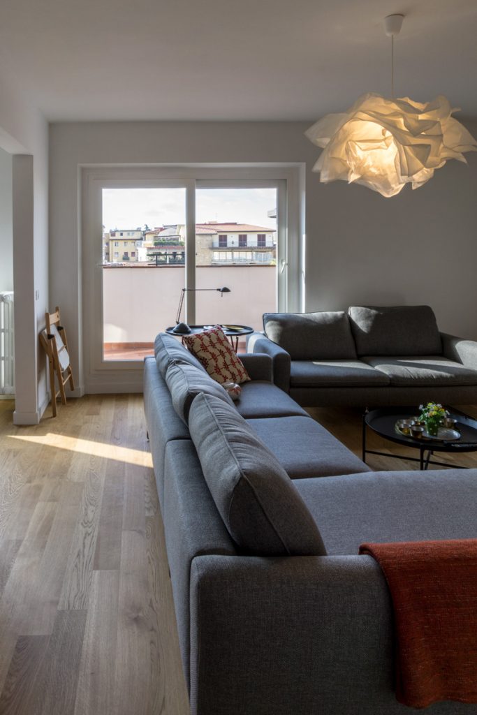 Casa AJ - Zona soggiorno con pavimento in legno, divani di colore grigio, infissi ad ante scorrevoli e lampada in policarbonato - Tommaso Vecci